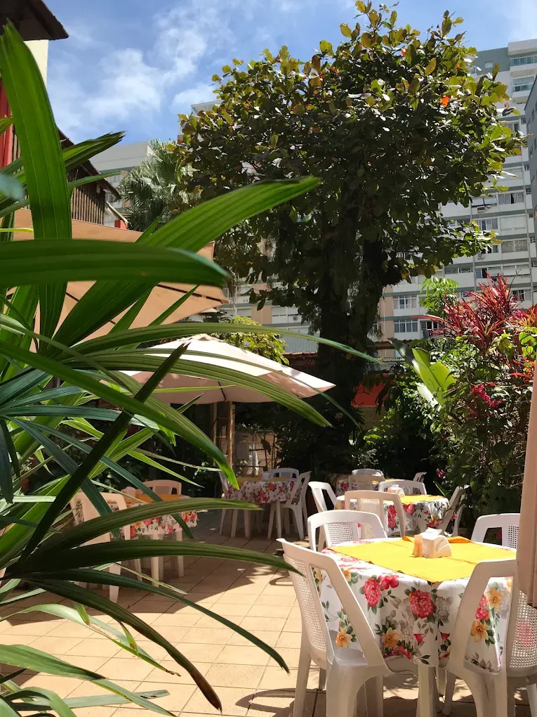 Quintal ensolarado com mesas de toalha floral e guarda-sóis